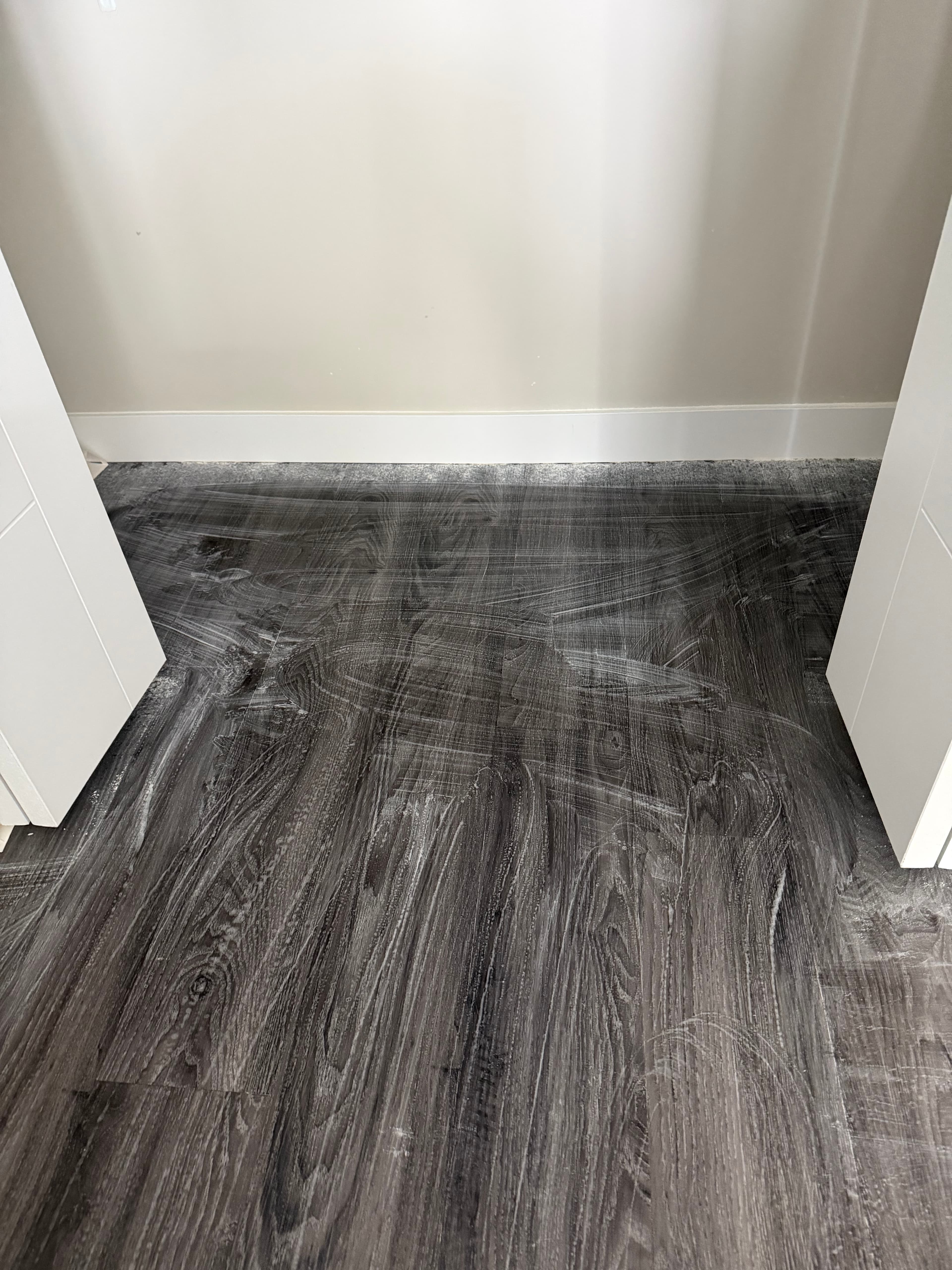 Dark wood-look floor covered in white, streaky residue between two white door frames.