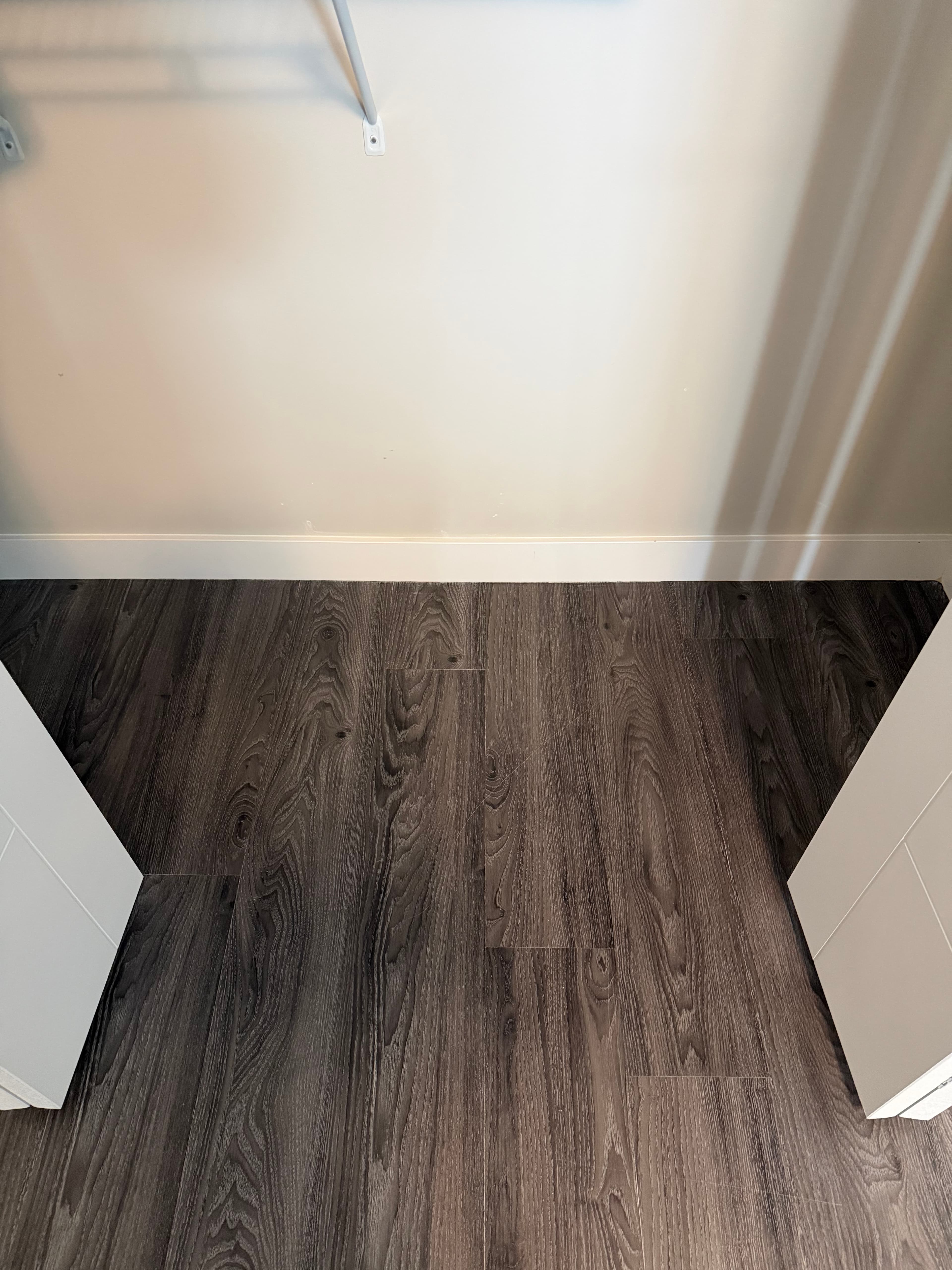Dark grey wood-look plank flooring inside a closet with white walls and baseboards.