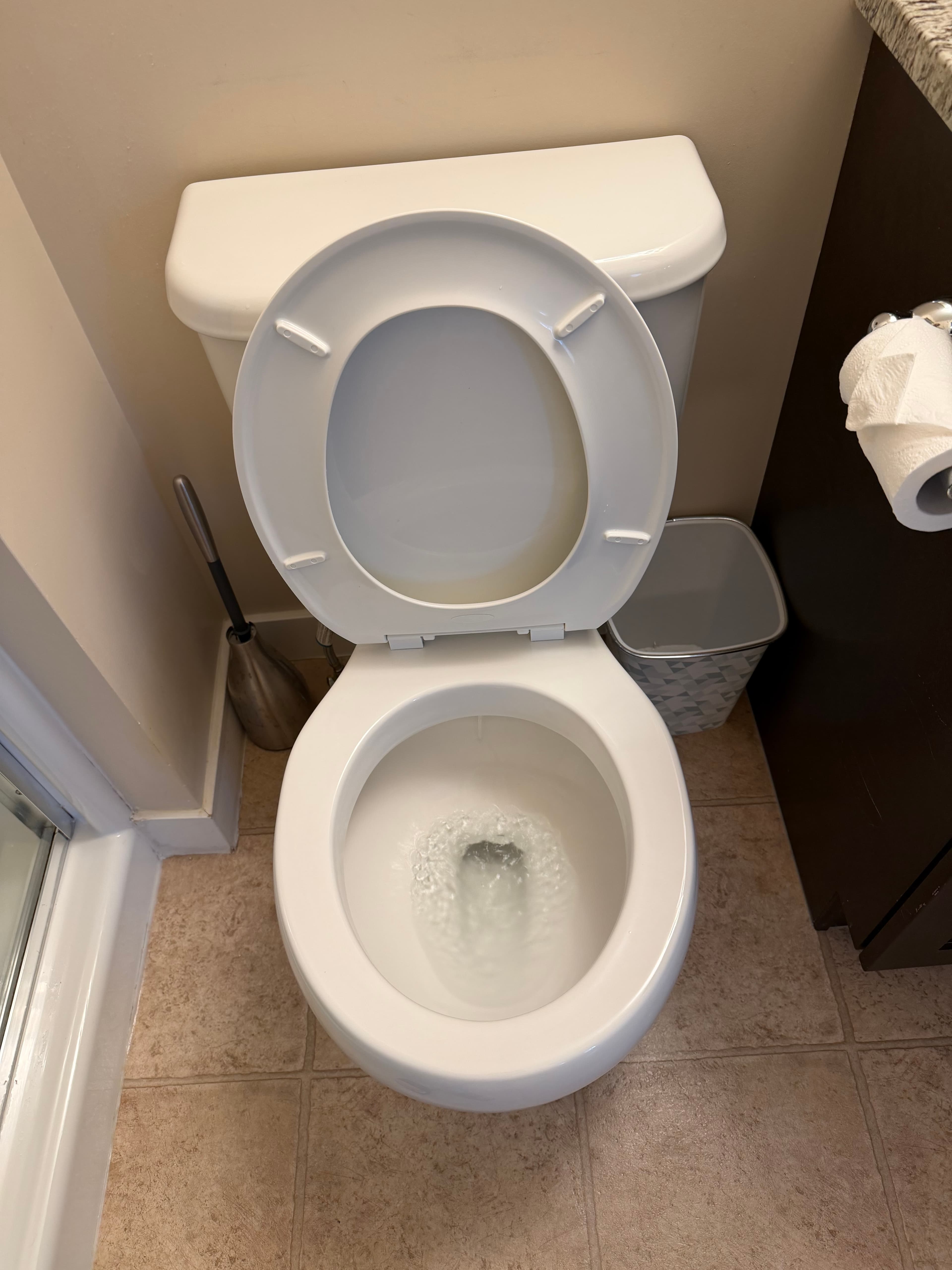 White toilet with open lid and seat, showing water swirling in the bowl while flushing.